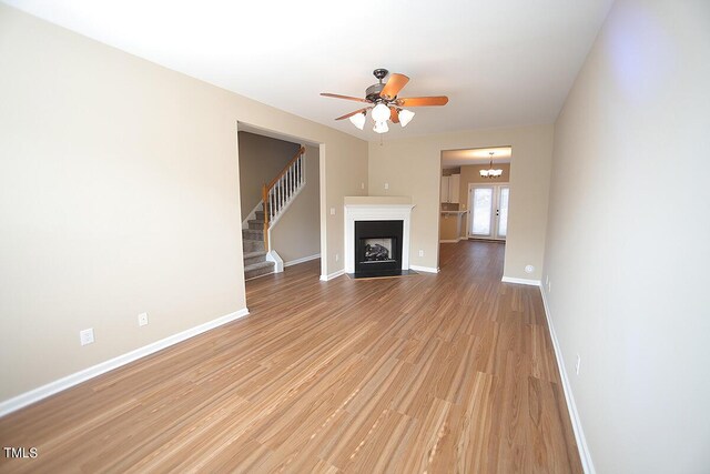 unfurnished living room with ceiling fan with notable chandelier and light wood-type flooring