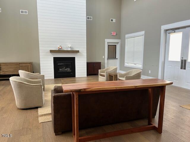 living room featuring light wood-type flooring, a towering ceiling, and a fireplace