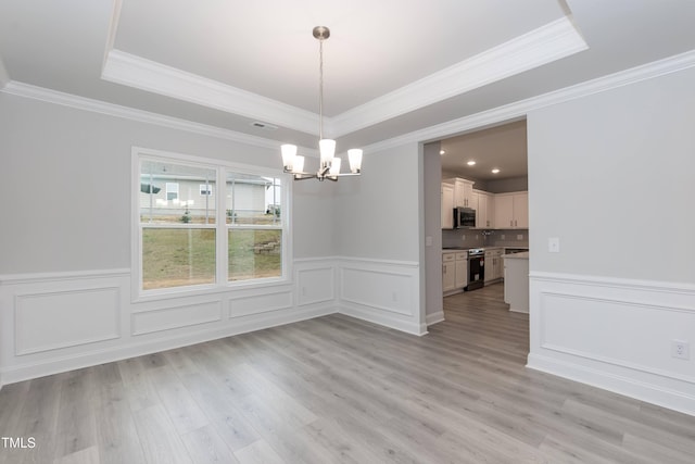 unfurnished dining area featuring a raised ceiling, crown molding, light wood-type flooring, and an inviting chandelier