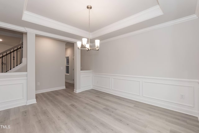 unfurnished dining area with a raised ceiling, ornamental molding, light hardwood / wood-style floors, and an inviting chandelier