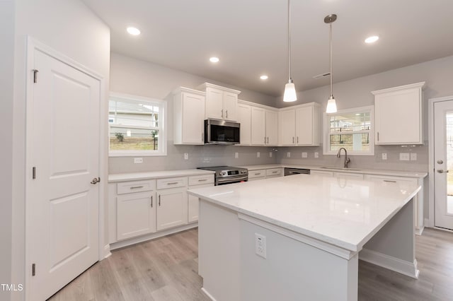 kitchen with a center island, white cabinets, sink, appliances with stainless steel finishes, and decorative light fixtures