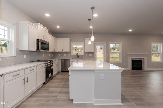 kitchen with white cabinetry, a center island, stainless steel appliances, pendant lighting, and a fireplace