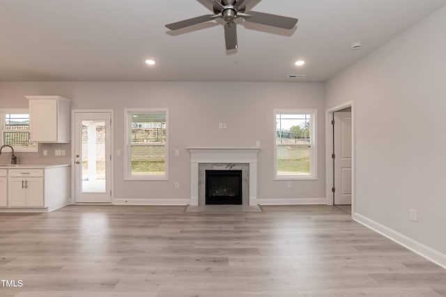 unfurnished living room with a wealth of natural light, a high end fireplace, light hardwood / wood-style floors, and ceiling fan