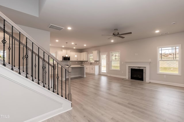 unfurnished living room with a fireplace, ceiling fan, sink, and light hardwood / wood-style floors