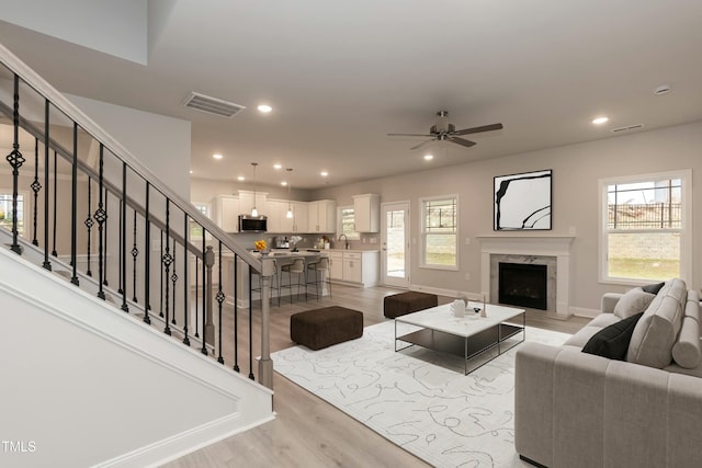 living room with a fireplace, ceiling fan, sink, and light hardwood / wood-style floors