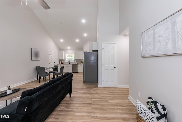 living room featuring high vaulted ceiling, sink, and light hardwood / wood-style floors