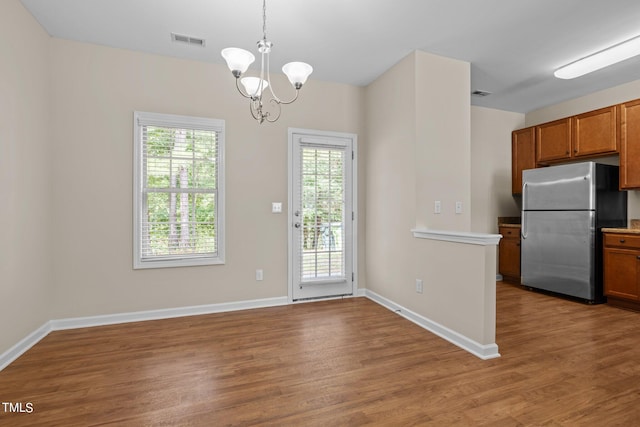 kitchen with decorative light fixtures, stainless steel refrigerator, an inviting chandelier, and wood-type flooring