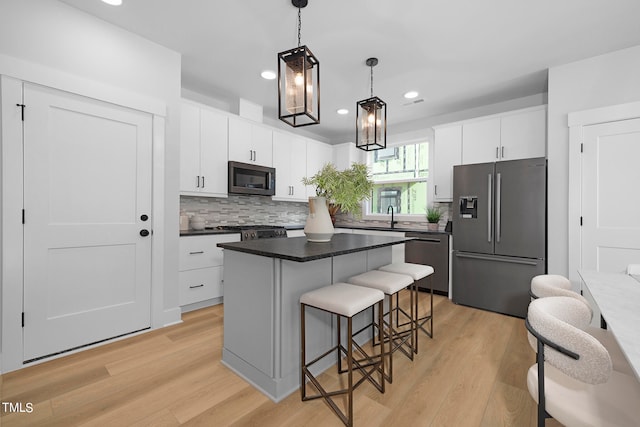 kitchen featuring appliances with stainless steel finishes, white cabinetry, hanging light fixtures, light hardwood / wood-style floors, and a kitchen island