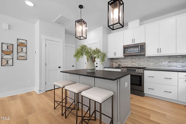 kitchen with appliances with stainless steel finishes, a center island, hanging light fixtures, and white cabinets