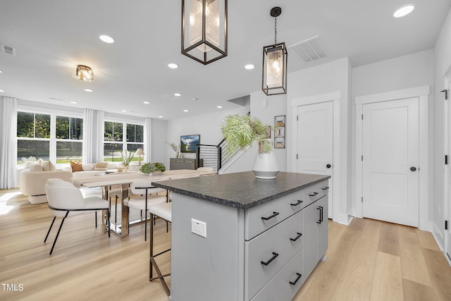 kitchen with a breakfast bar area, decorative light fixtures, a kitchen island, and light hardwood / wood-style flooring