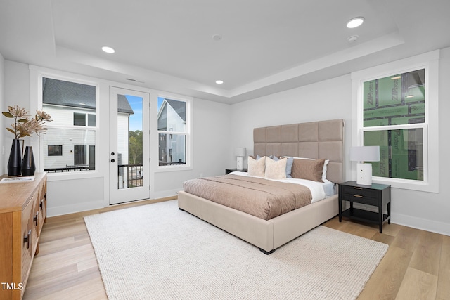 bedroom featuring a tray ceiling, access to exterior, and light hardwood / wood-style flooring