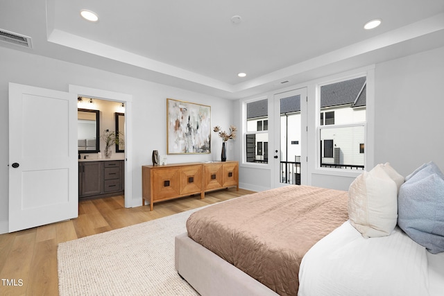 bedroom featuring ensuite bathroom, a tray ceiling, access to exterior, and light wood-type flooring