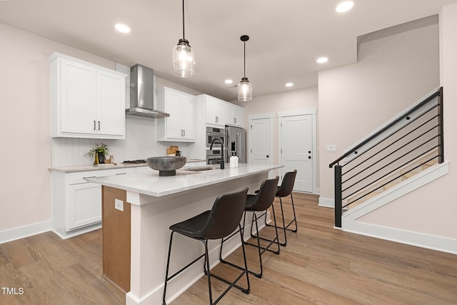 kitchen with wall chimney range hood, white cabinets, and an island with sink