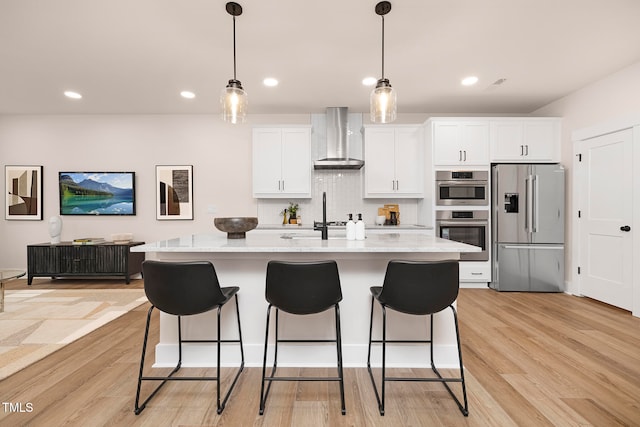 kitchen featuring white cabinetry, a center island with sink, appliances with stainless steel finishes, tasteful backsplash, and wall chimney exhaust hood