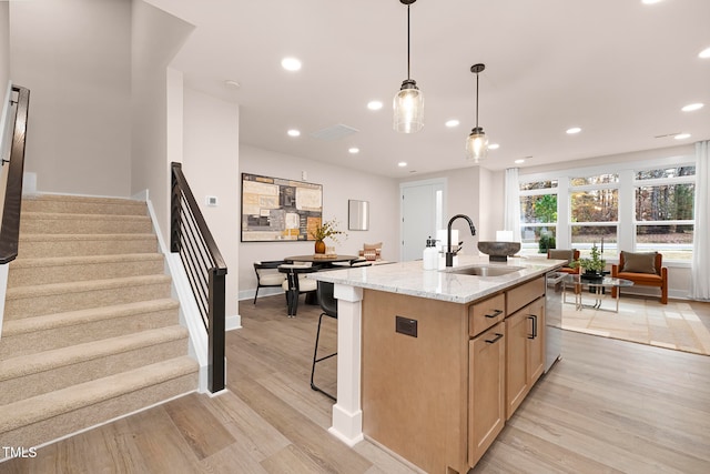 kitchen with light stone countertops, an island with sink, sink, stainless steel dishwasher, and light hardwood / wood-style flooring