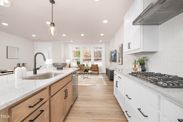 kitchen with wall chimney range hood, sink, appliances with stainless steel finishes, light brown cabinets, and white cabinets