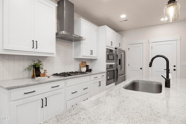 kitchen featuring wall chimney range hood, sink, appliances with stainless steel finishes, white cabinets, and light stone counters