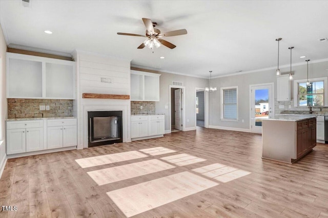 unfurnished living room featuring a large fireplace, ceiling fan with notable chandelier, baseboards, ornamental molding, and light wood-type flooring