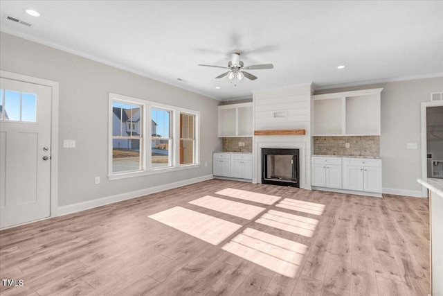 unfurnished living room with light wood finished floors, visible vents, crown molding, a fireplace, and a wealth of natural light