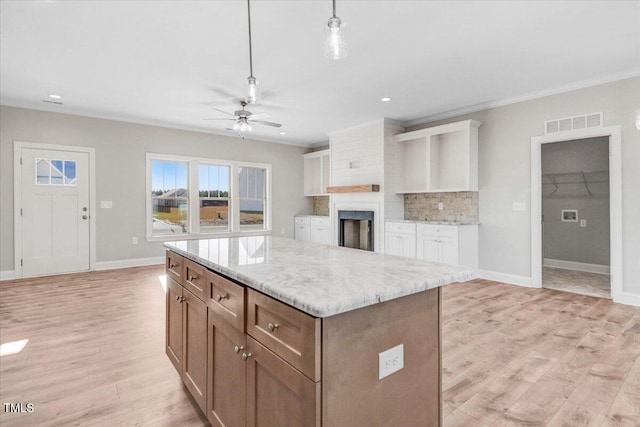 kitchen featuring a center island, tasteful backsplash, light wood-style flooring, ornamental molding, and baseboards