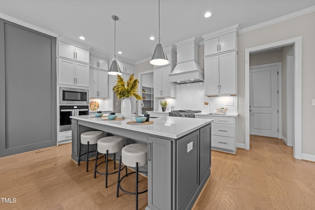 kitchen with a kitchen bar, decorative light fixtures, a center island with sink, custom range hood, and stainless steel appliances