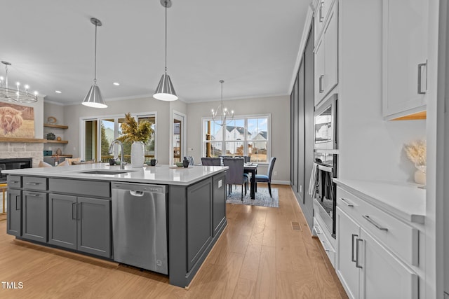 kitchen with hanging light fixtures, gray cabinets, an island with sink, stainless steel appliances, and a fireplace