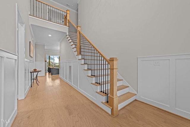 stairs with crown molding, a towering ceiling, and hardwood / wood-style floors