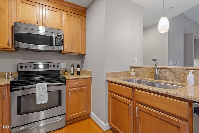 kitchen featuring appliances with stainless steel finishes, light hardwood / wood-style flooring, sink, light stone counters, and decorative light fixtures