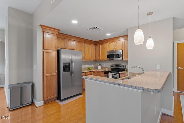 kitchen with sink, appliances with stainless steel finishes, light wood-type flooring, and kitchen peninsula