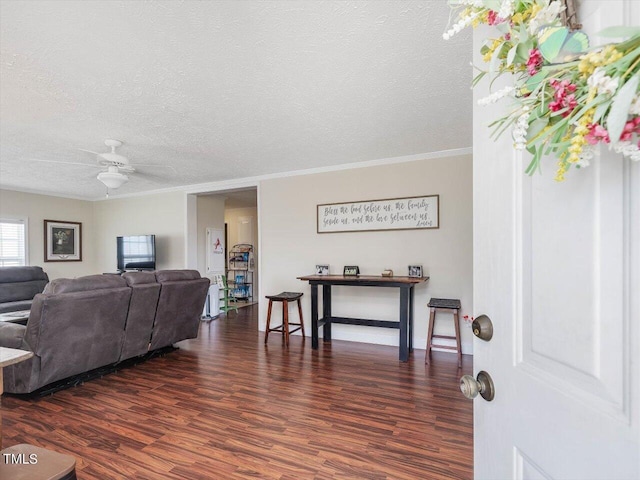 living room featuring ceiling fan, ornamental molding, dark hardwood / wood-style flooring, and a textured ceiling