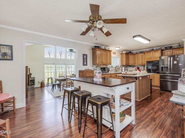 kitchen with a kitchen island, oven, a textured ceiling, and stainless steel refrigerator with ice dispenser