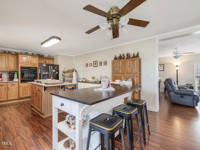 kitchen featuring crown molding, black oven, a center island, stainless steel refrigerator with ice dispenser, and a textured ceiling