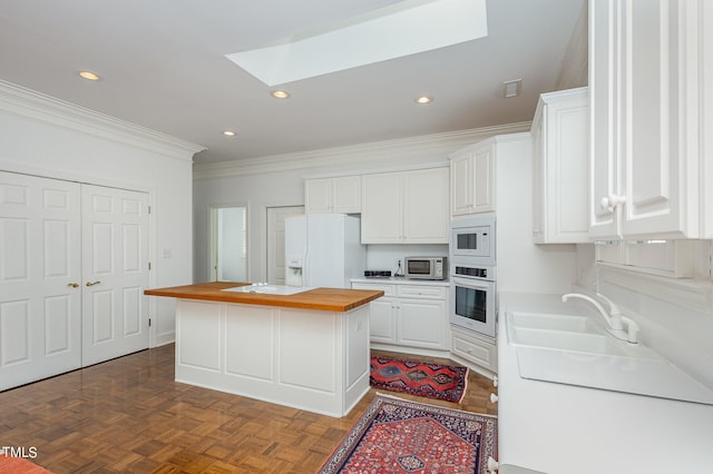 kitchen with white appliances, white cabinets, a center island, wood counters, and parquet flooring