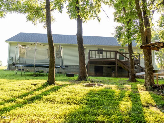 rear view of property featuring a wooden deck, a lawn, and a trampoline