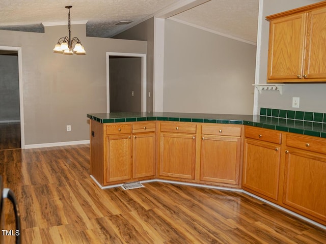 kitchen with tile countertops, wood-type flooring, kitchen peninsula, a textured ceiling, and a chandelier