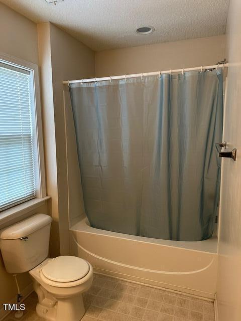 bathroom featuring tile patterned flooring, toilet, shower / tub combo, and a textured ceiling