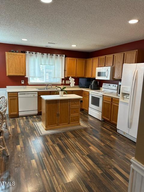 kitchen with dark wood-type flooring, a textured ceiling, sink, and white appliances