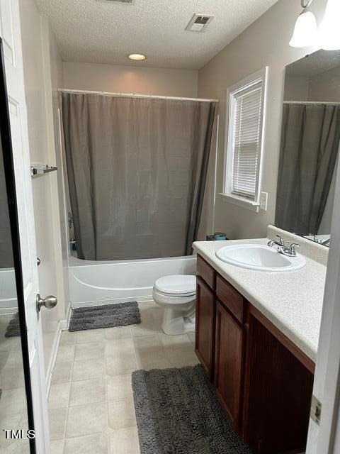 full bathroom featuring tile patterned flooring, a textured ceiling, toilet, vanity, and shower / tub combo with curtain