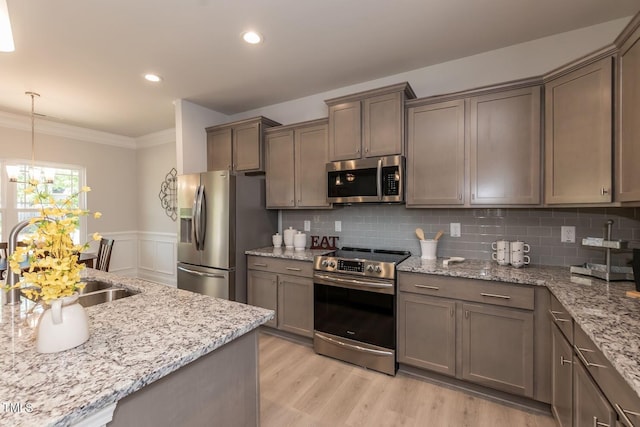 kitchen with stainless steel appliances, light wood-style floors, ornamental molding, wainscoting, and a sink