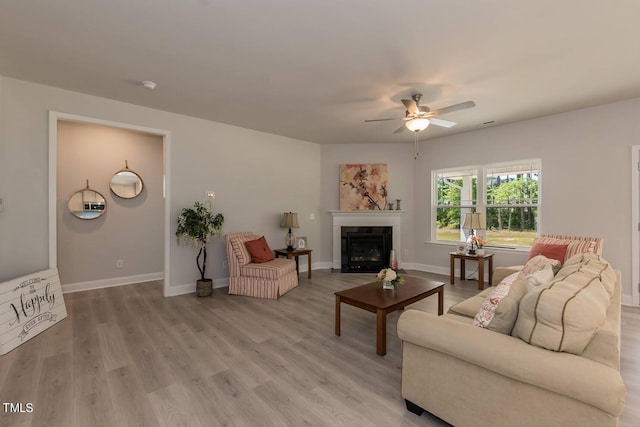 living room featuring a fireplace with flush hearth, light wood-style flooring, baseboards, and a ceiling fan