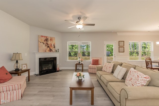 living area with a ceiling fan, a glass covered fireplace, baseboards, and light wood finished floors