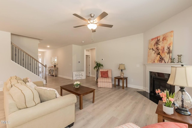 living room with light wood-style floors, baseboards, stairway, and a fireplace with raised hearth