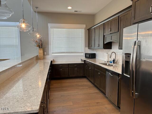 kitchen with decorative backsplash, appliances with stainless steel finishes, a sink, dark brown cabinets, and light wood-type flooring