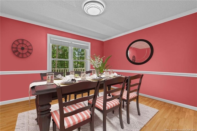 dining space with light wood-type flooring, ornamental molding, and a textured ceiling