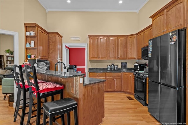 kitchen with black appliances, a kitchen breakfast bar, ornamental molding, and light hardwood / wood-style flooring