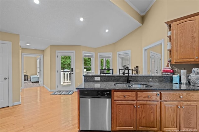 kitchen with lofted ceiling, dark stone countertops, stainless steel dishwasher, sink, and light hardwood / wood-style flooring