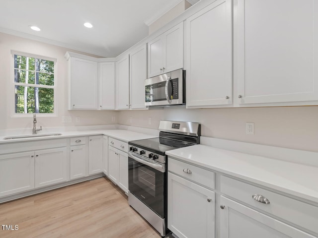 kitchen with appliances with stainless steel finishes, sink, white cabinetry, crown molding, and light hardwood / wood-style flooring