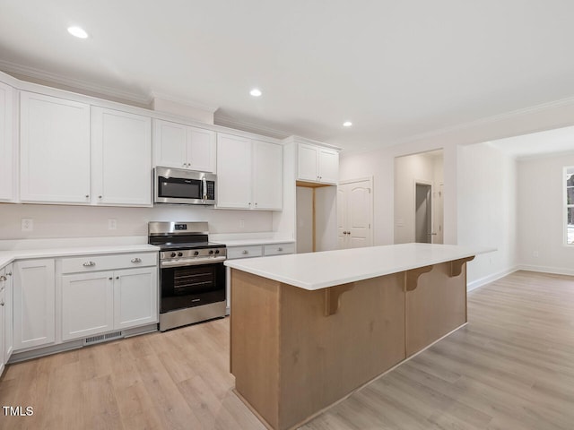 kitchen with ornamental molding, stainless steel appliances, a center island, and light wood-type flooring