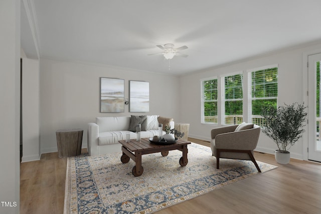 living room featuring ornamental molding, light wood-style flooring, baseboards, and a ceiling fan