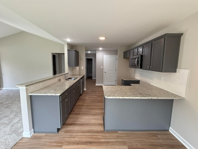 kitchen with light stone counters, sink, kitchen peninsula, light hardwood / wood-style flooring, and backsplash